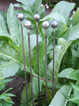 Handmade naturally rusting metal ball stake with spherical finial for garden borders.